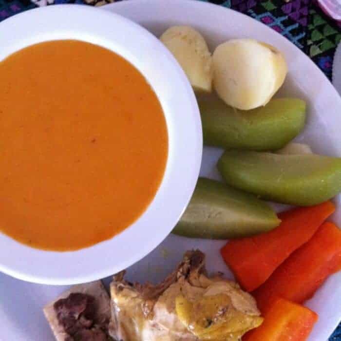 A plate of Guatemalan pulique with chicken meat and vegetables on the side. 