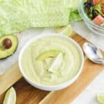 Creamy avocado lime dressing in a carafe with green salad in background.
