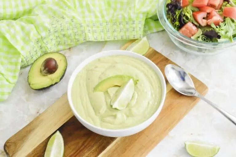 Avocado sauce in a white bowl on a wooden board.