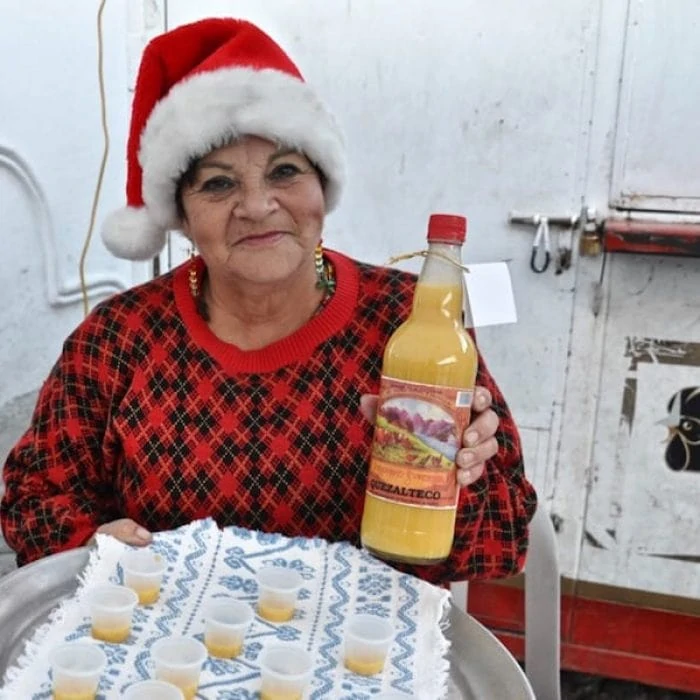 Woman wearing a Santa hat holding a bottle of rompope.