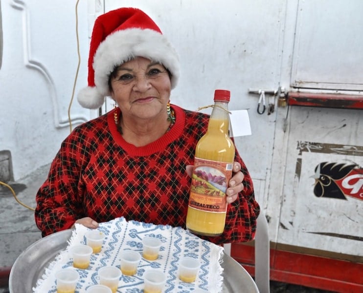 A woman with a Santa hat holding a bottle of Rompopo, an eggnog produced in Salcajá, Quetzaltenango. 