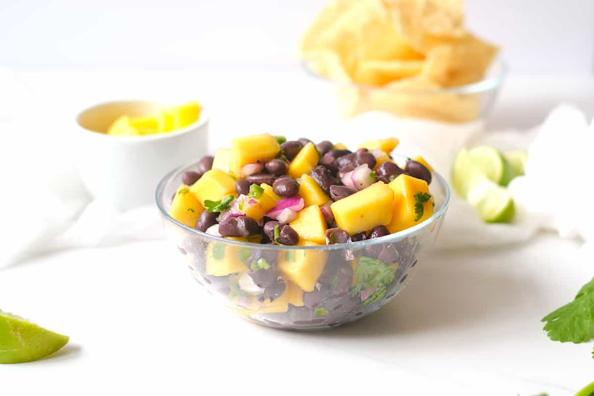 Mango black bean salad on a white table with limes and cilantro. 