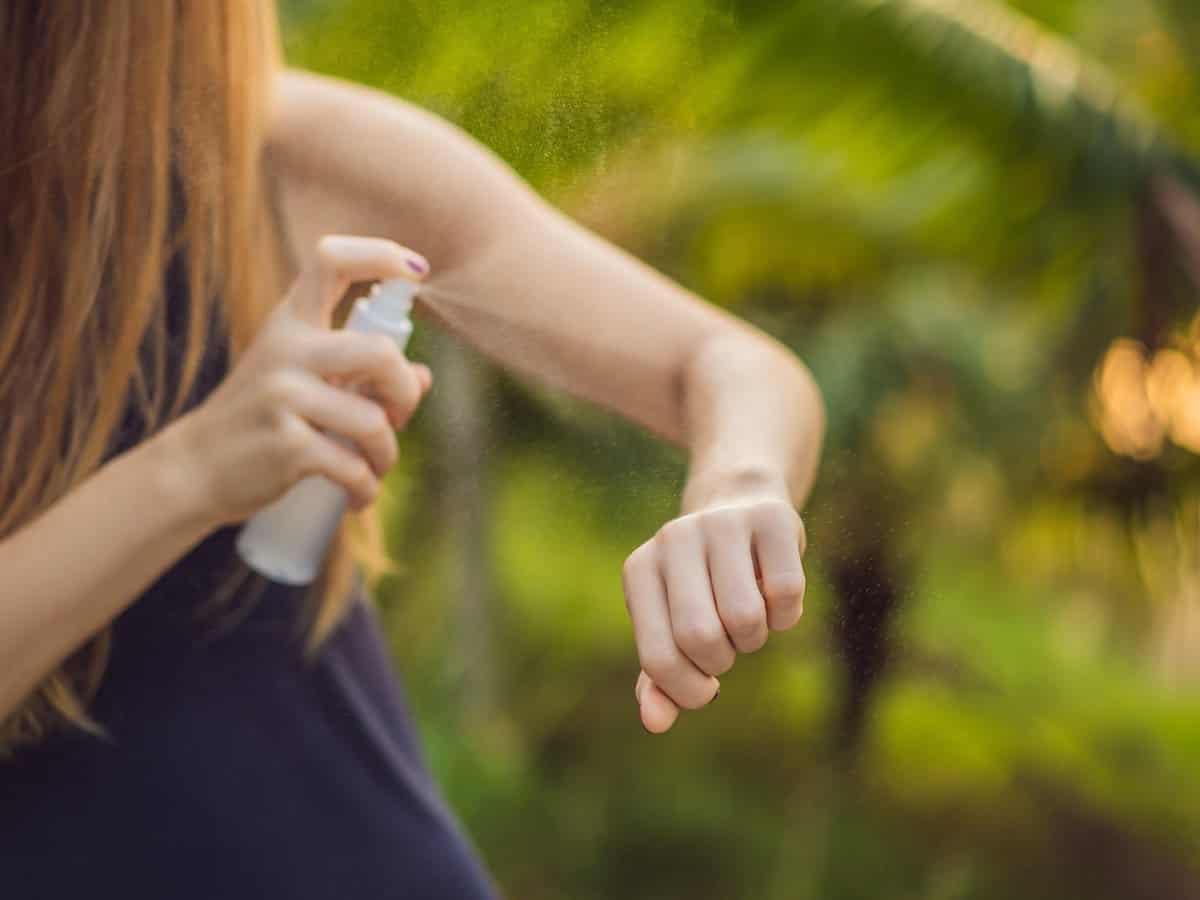 Close-up of a woman spraying insect repellent on her arms. 