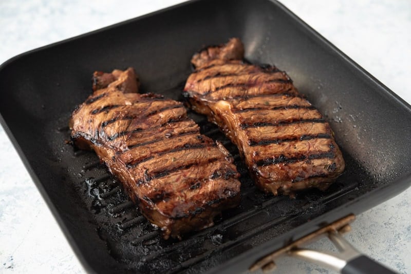 Two marinated steaks grilling in a cast iron pan. 