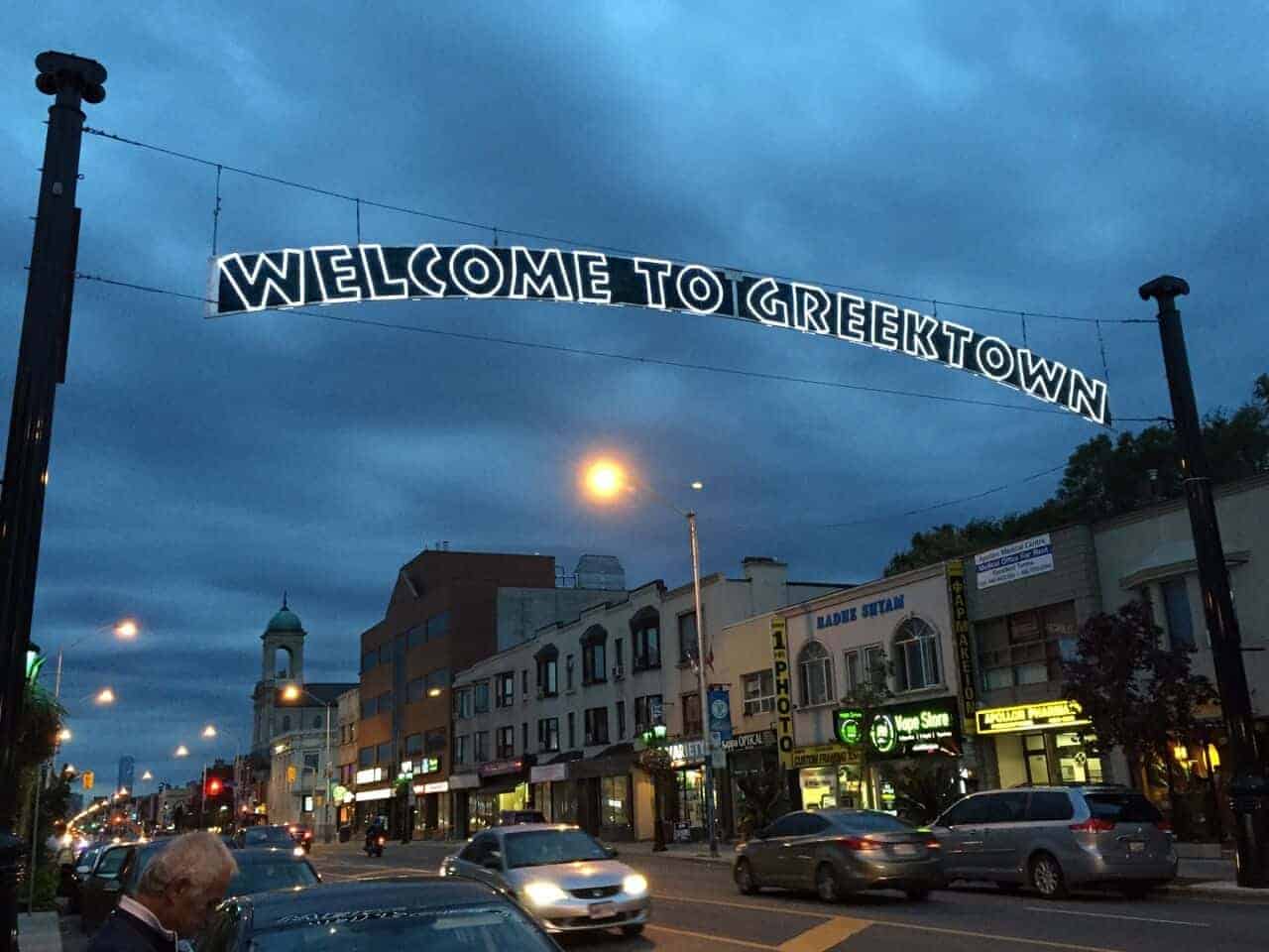 Illuminated Welcome to Greektown sign in Toronto at night.