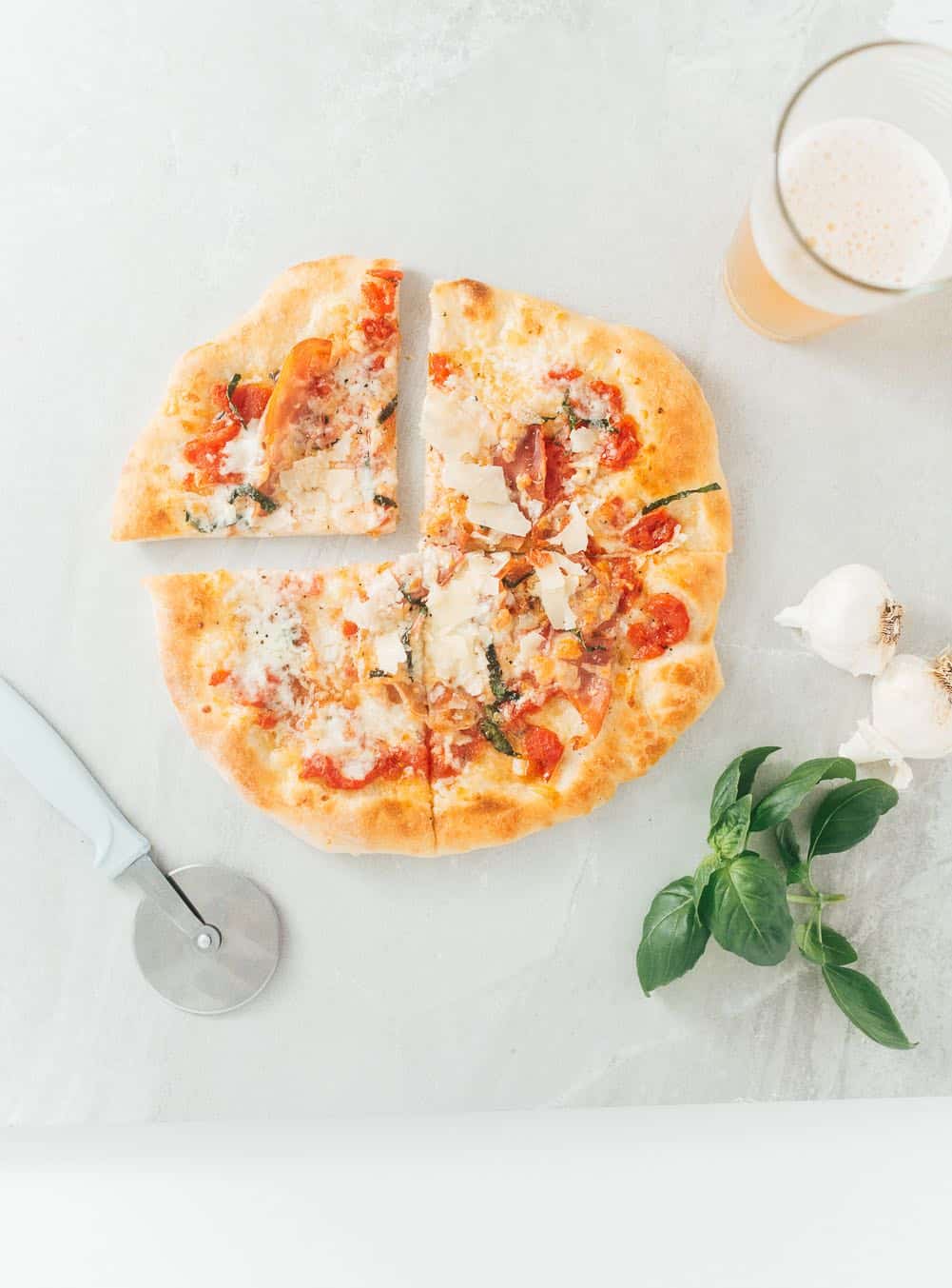 Pizza dough with cutter and fresh basil on a table.