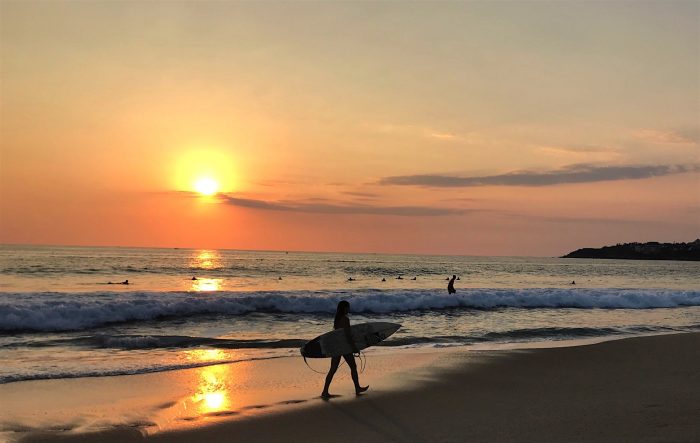 Female walking with surfboard at sunset in Puerto Escondido, Oaxaca. 