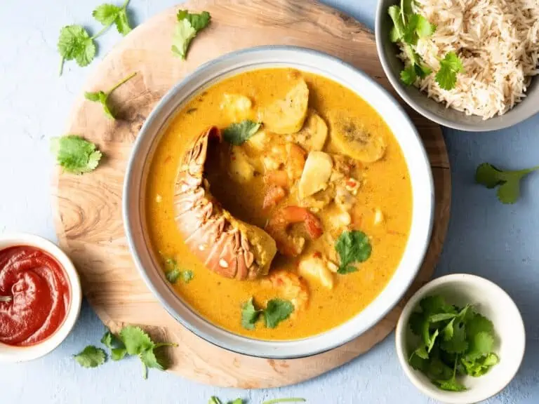 A white bowl of Garifuna tapado seafood soup from Guatemala with rice on the side. .