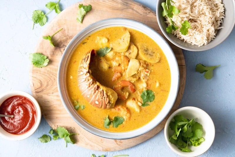 Tapado, a Guatemalan seafood soup with coconut milk, yucca and plantain in a white bowls on a wooden board. 