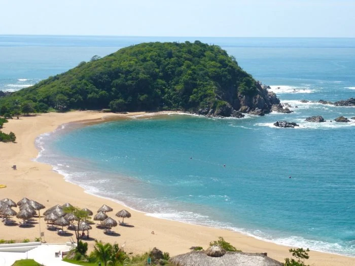 View of Conejos Bay from the resort with beach palapas on the sand. 