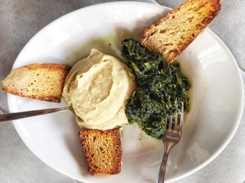 Purè di fave e cicorie or Fava Bean Purée with Chicory on a white plate with crostini. 