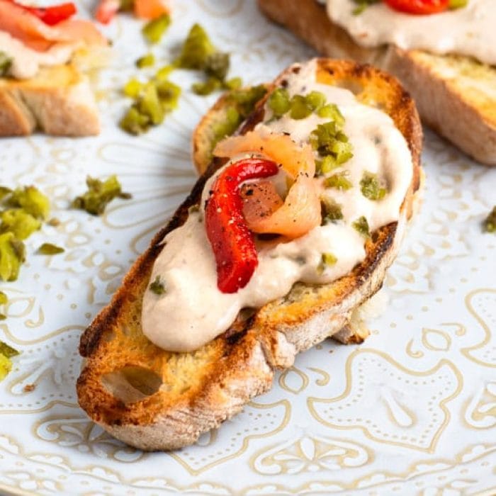 Creamed sardines topped with smoked salmon on crostini on a white plate. 