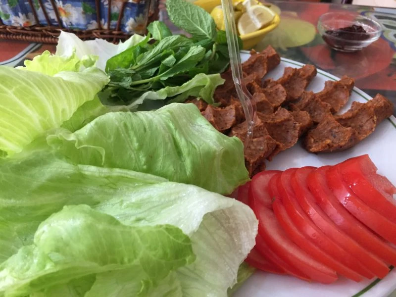 Lettuce, tomatoes and traditional cig kofte on a white plate. 