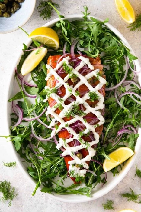 Smoked Trout Platter with Fresh Herbs, Lemon and Horseradish Cream Sauce on a white platter. 