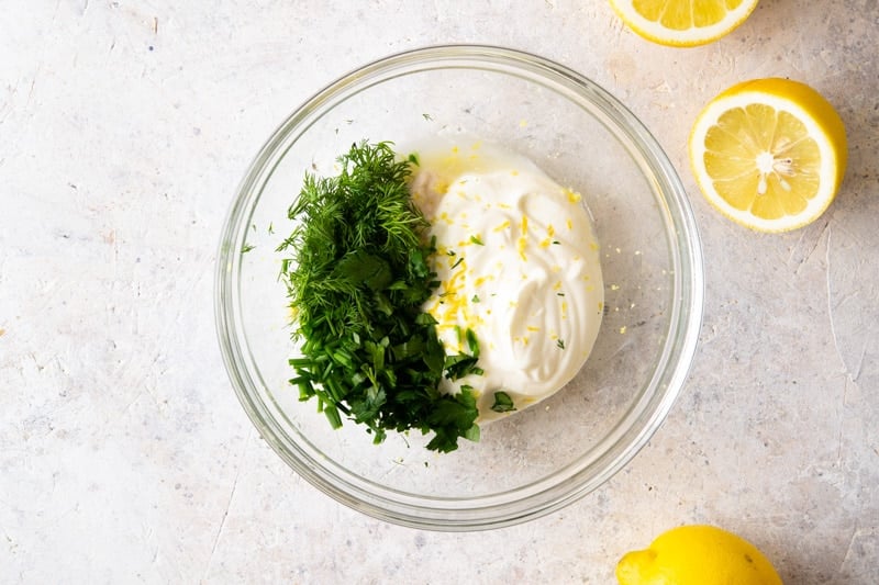 Mixture of sour cream, dill and chopped chives in a glass bowl. 