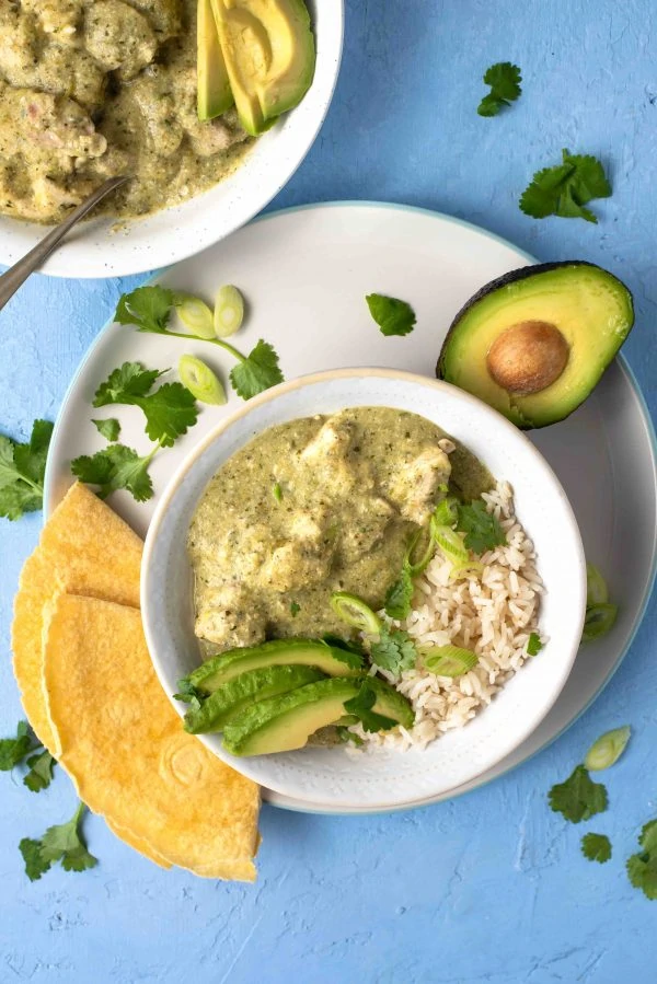 Chicken in green tomatillo salsa or pollo jocon in a white dish with avocado. 