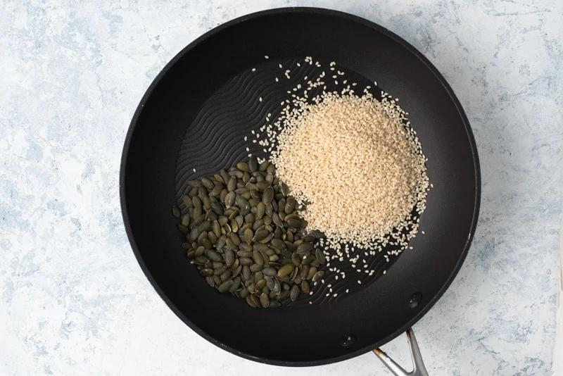 Toasting pepitoria and sesame seeds in a skillet. 