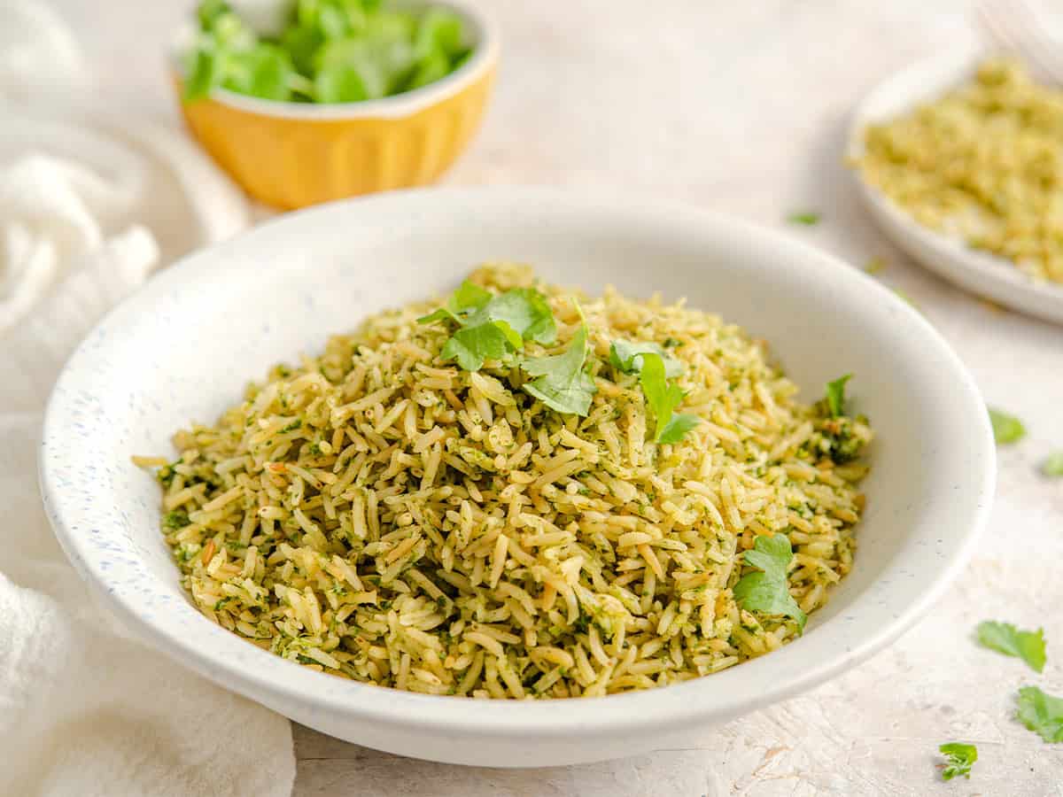 A bowl of Mexican green rice on the table with a bowl of cilantro leaves.