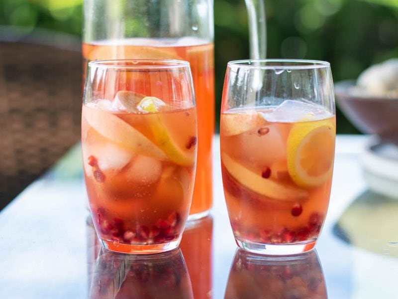 A pitcher and two glasses of Bourbon Peach Punch with Pomegranate.