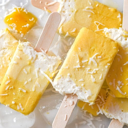Mango coconut popsicles on a white table.