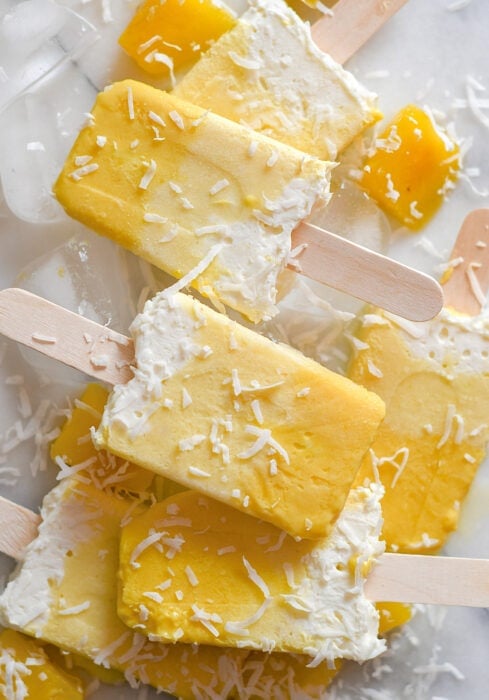 Pina Colada and Mango Popsicles on a white background sprinkled with coconut flakes. 