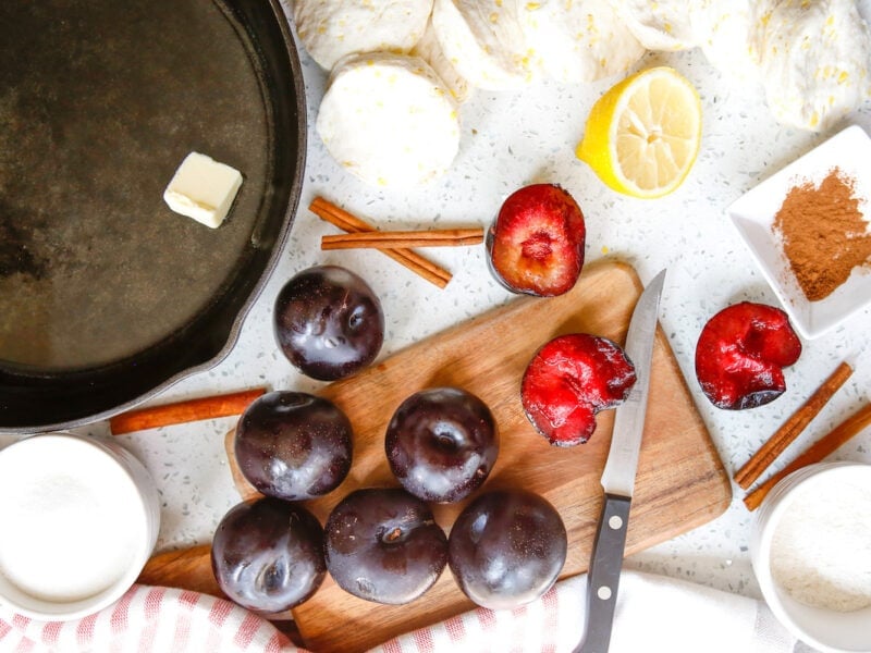 Plums on cutting board with other ingredients for plum cobbler 