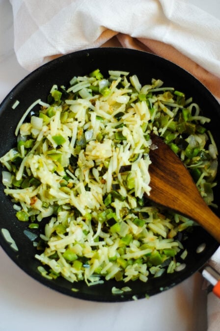 Shredded peppers and onions in a cast iron pan.