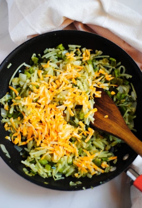 Shredded cheese being added to a pan with hash browns and peppers to make a meatless breakfast casserole.