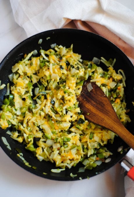 The Spanish breakfast casserole ingredients fully cooked and mixed - hash browns, peppers and cheese in a cast iron skillet. 