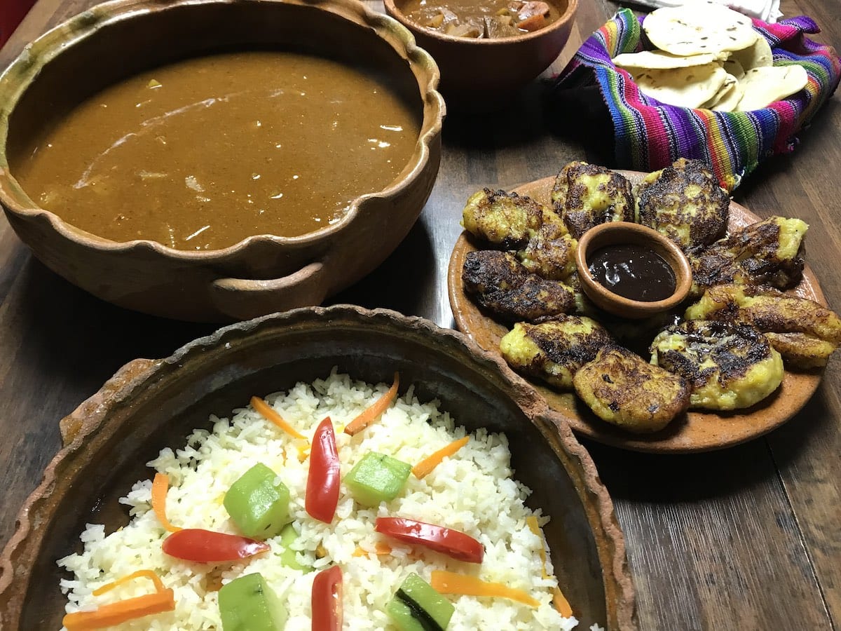 Traditional Guatemalan pepian, rice and rellenitos de platano in clay serving dishes on a table.