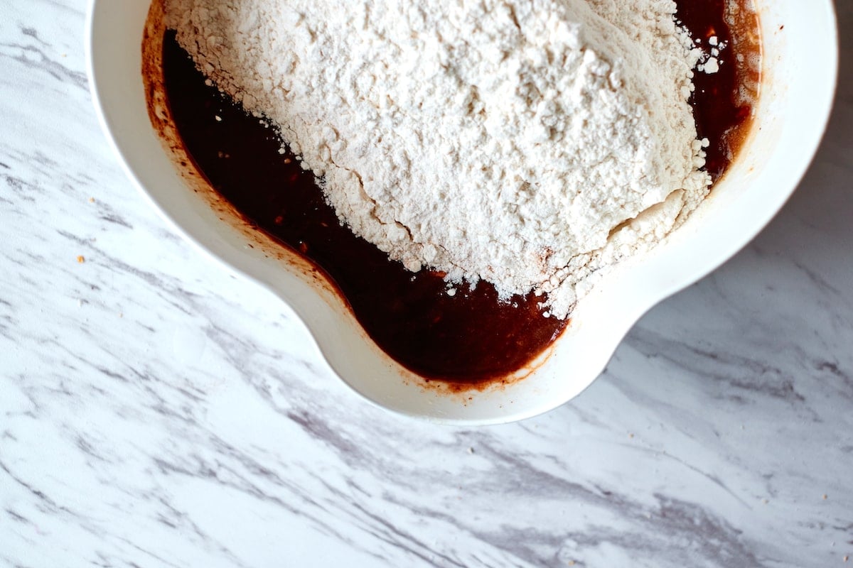 White flour being added to chocolate mixture in a white bowl.