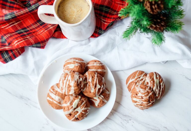 A plate of cookies with eggnog glaze on a white plate with a mug of hot chocolate.