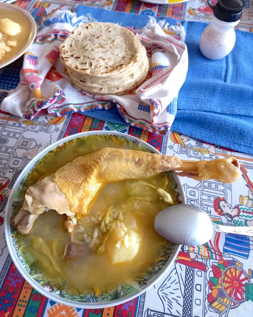 Chicken with loroco soup in a bowl on a colourful tablecloth.