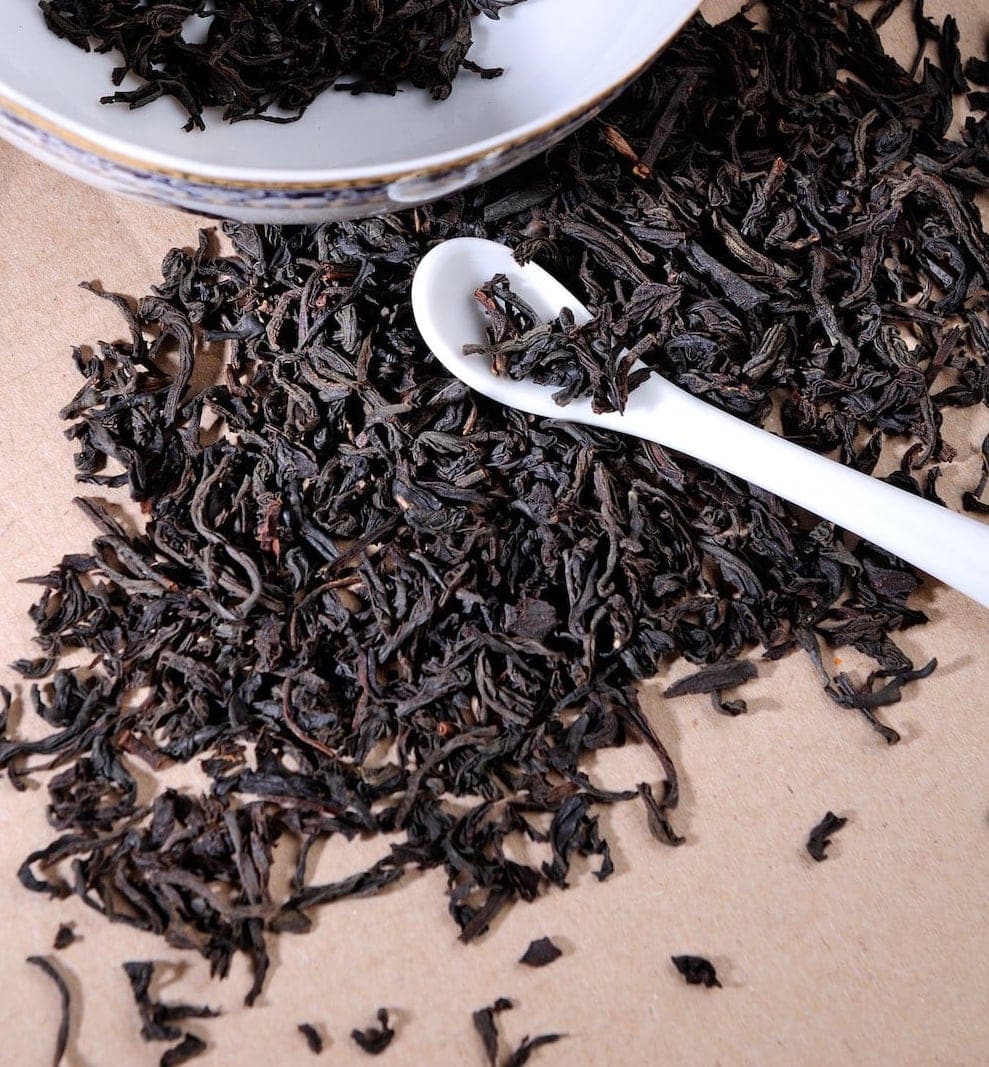 Dried black tea on a table with a white spoon.