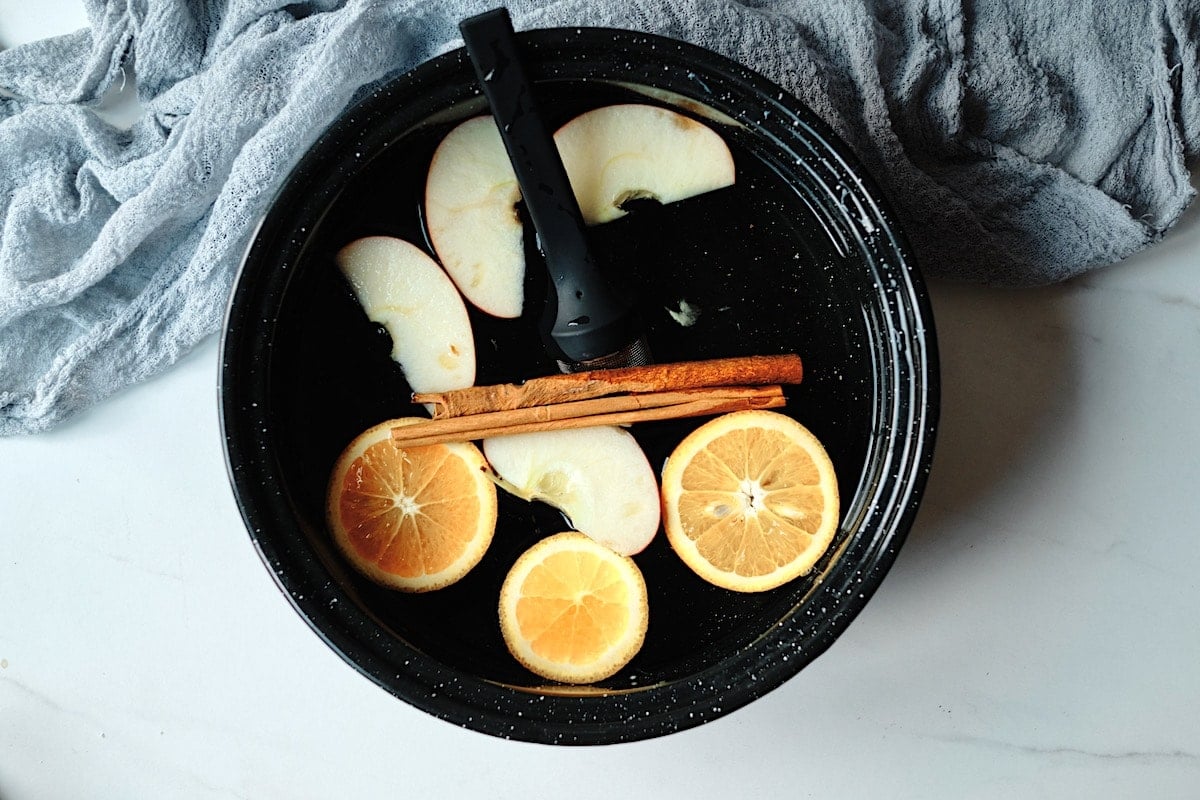 Black tea with orange, apple slices, the spices within an infuser and a cinnamon stick in a pot.