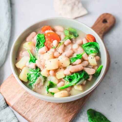Instant Pot white bean soup in a white bowl on a wooden tray.