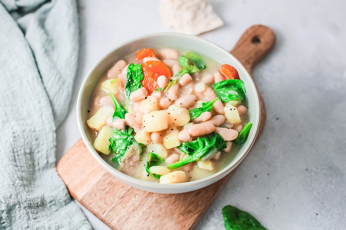 Instant Pot white bean soup in a white bowl on a wooden tray.