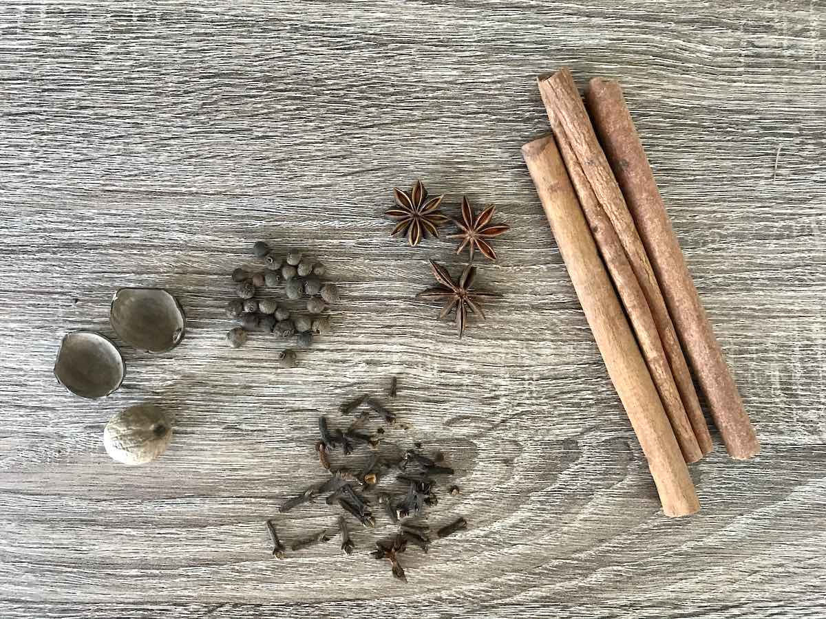 Cinnamon sticks, whole cloves, allspice, star anise and nutmeg on a wooden table.