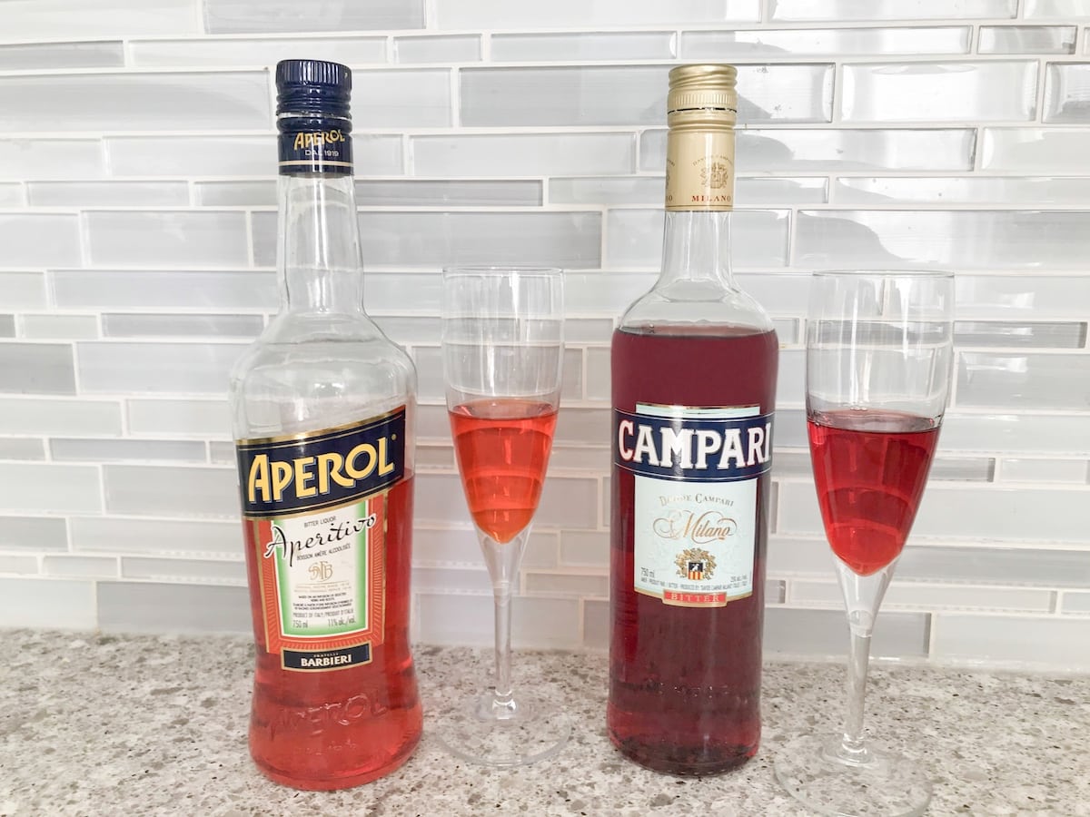 Differences in colour between orange Aperol and Red Campari demonstrated on two bottles and glasses of alcohol.