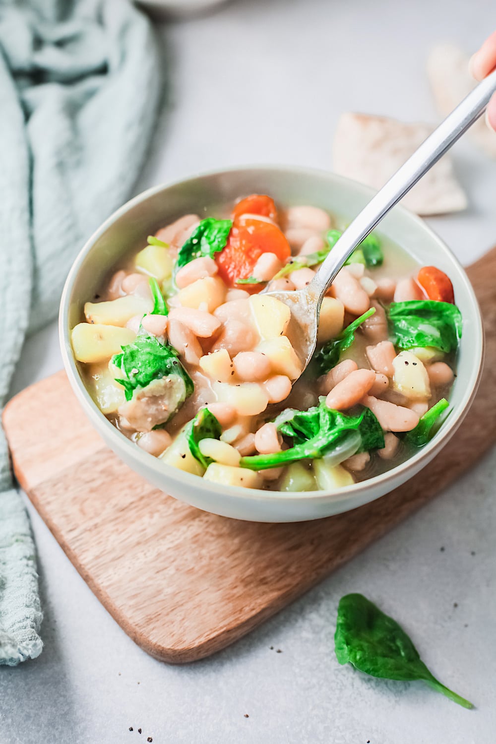 White bean soup with spinach and carrot in a white bowl on a wooden board. 