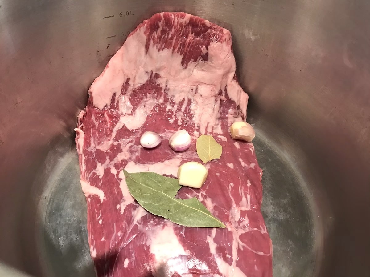 Flank steak in a stock pot with garlic and bay leaf.