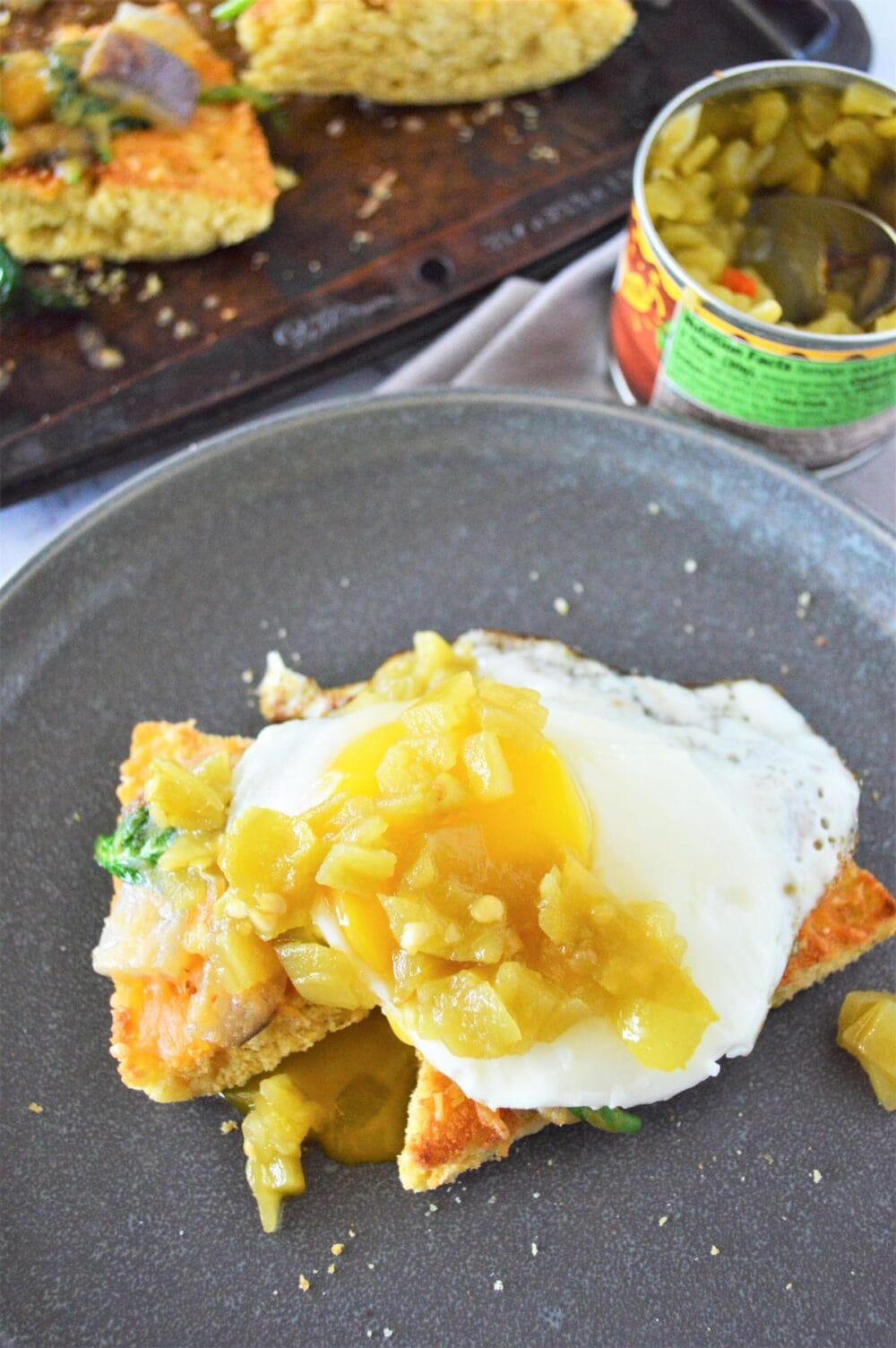 Open face cornbread breakfast sandwich of green chile eggs on toasted cornbread on a grey plate.