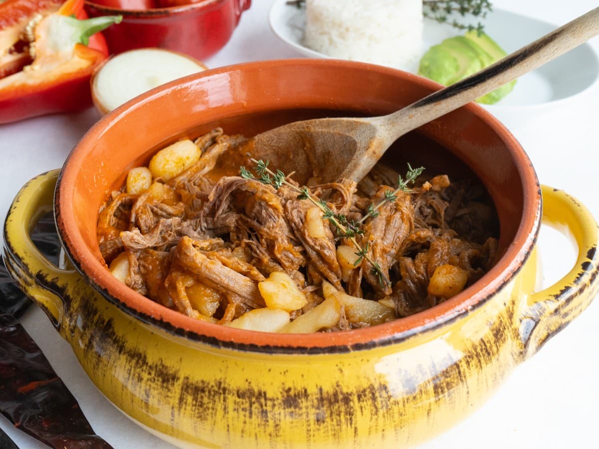 Guatemalan hilachas in a yellow bowl with a wooden spoon. 