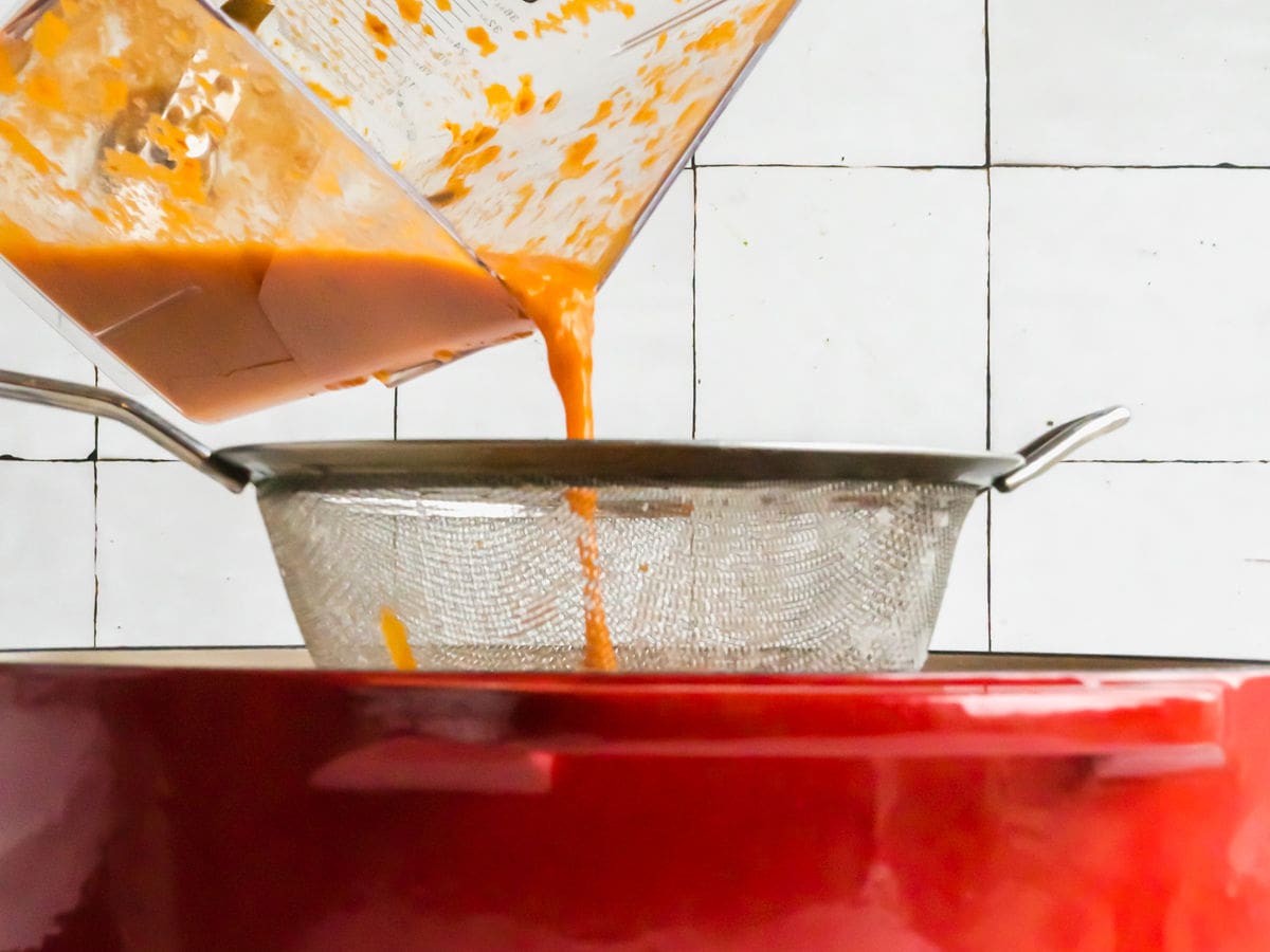 Straining tomato sauce into a Dutch Oven. 