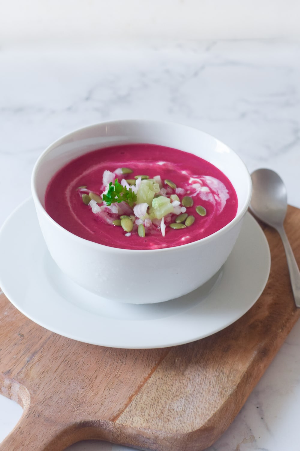 Beet gazpacho soup in a white bowl on a wooden board. 