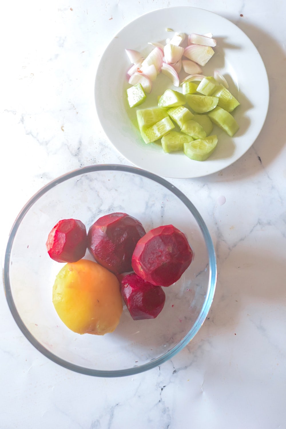 Cooked beets and potato with skins removed in a clear glass bowl.