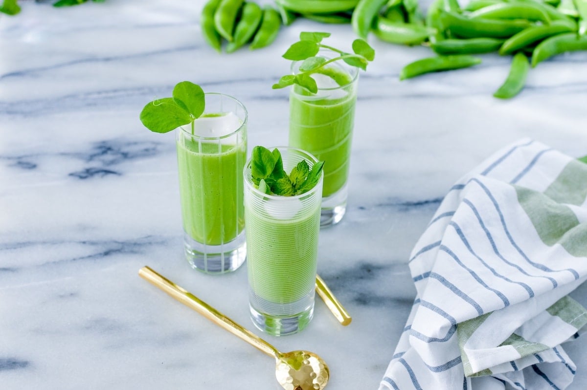 Three chilled pea gazpacho in shooter glasses on a marble table.