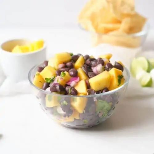 Clear bowl of mango black bean salsa on a white table.