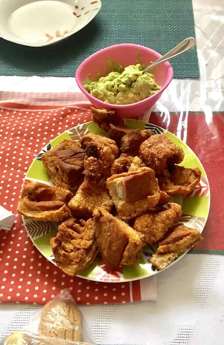 Crispy Guatemalan chicharrones on a plate with a bowl of guacamole.