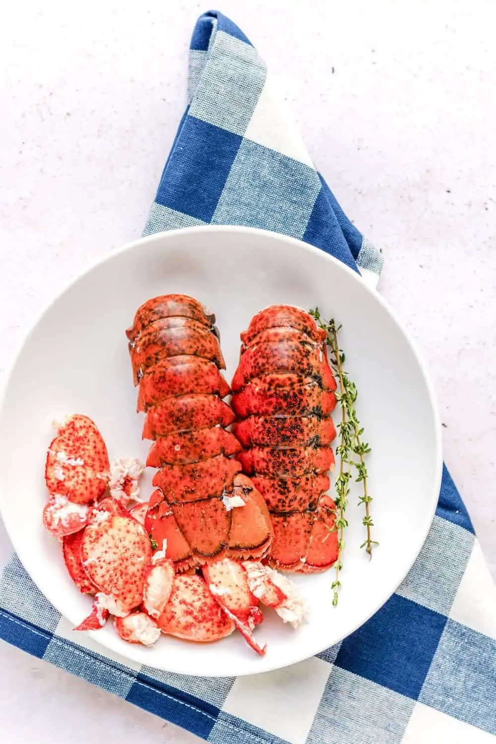 Cooked lobster tails and meat in a white bowl on a blue napkin.